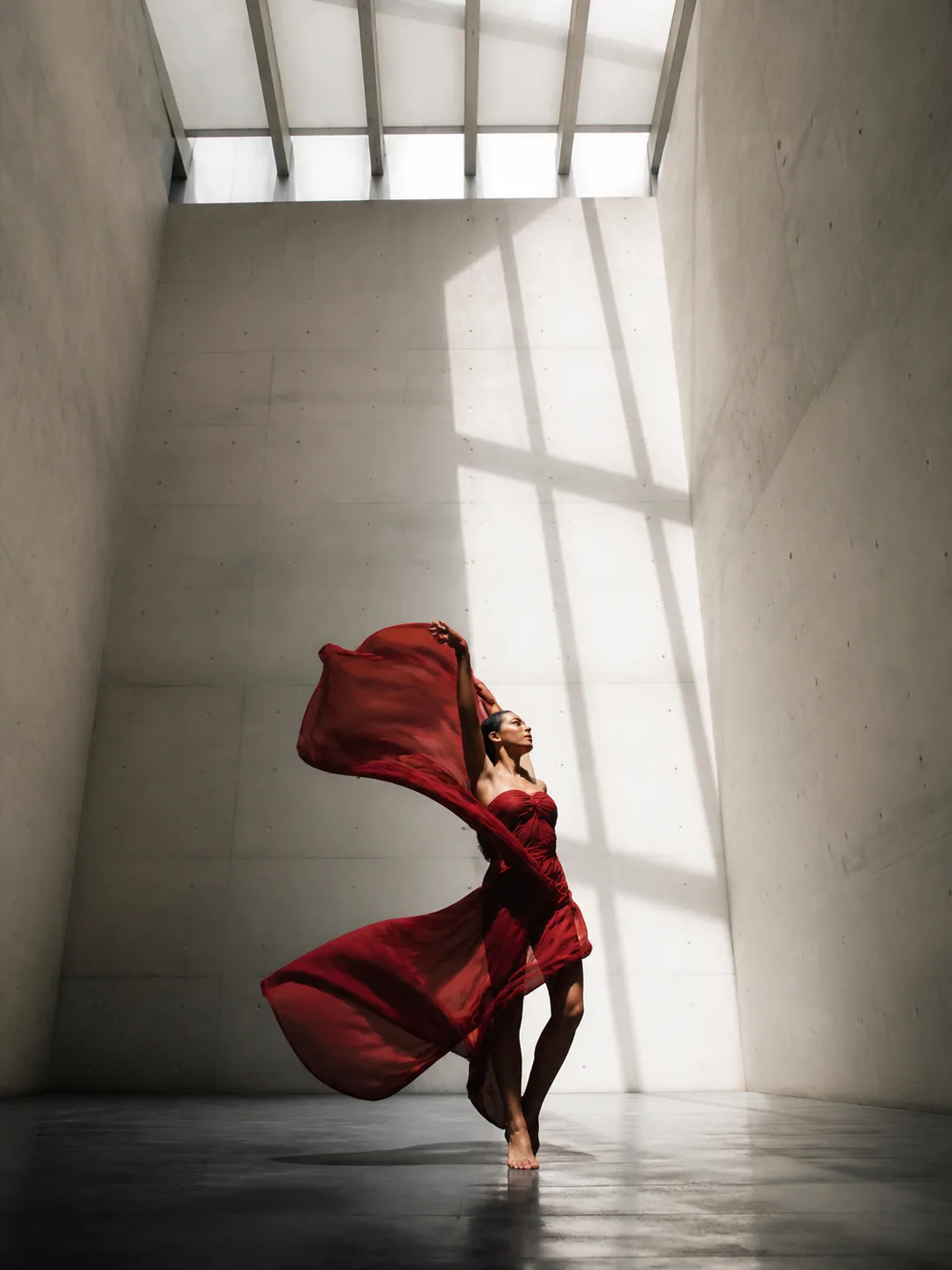 A dancer in red fabric inside a sunlit gallery